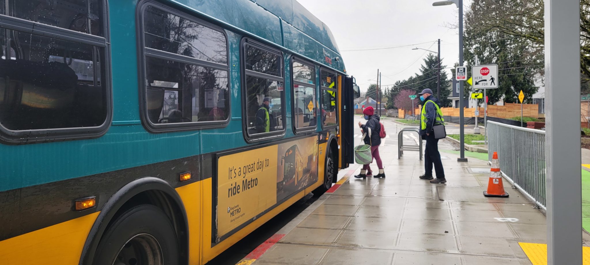 Two people board the bus at a new RapidRide-style bus stop along Delridge Way SW.