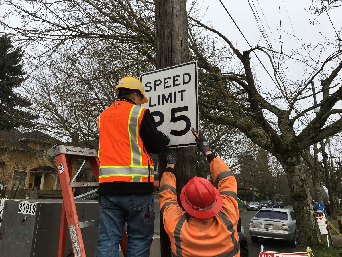 Two crew members replace a speed limit sign.
