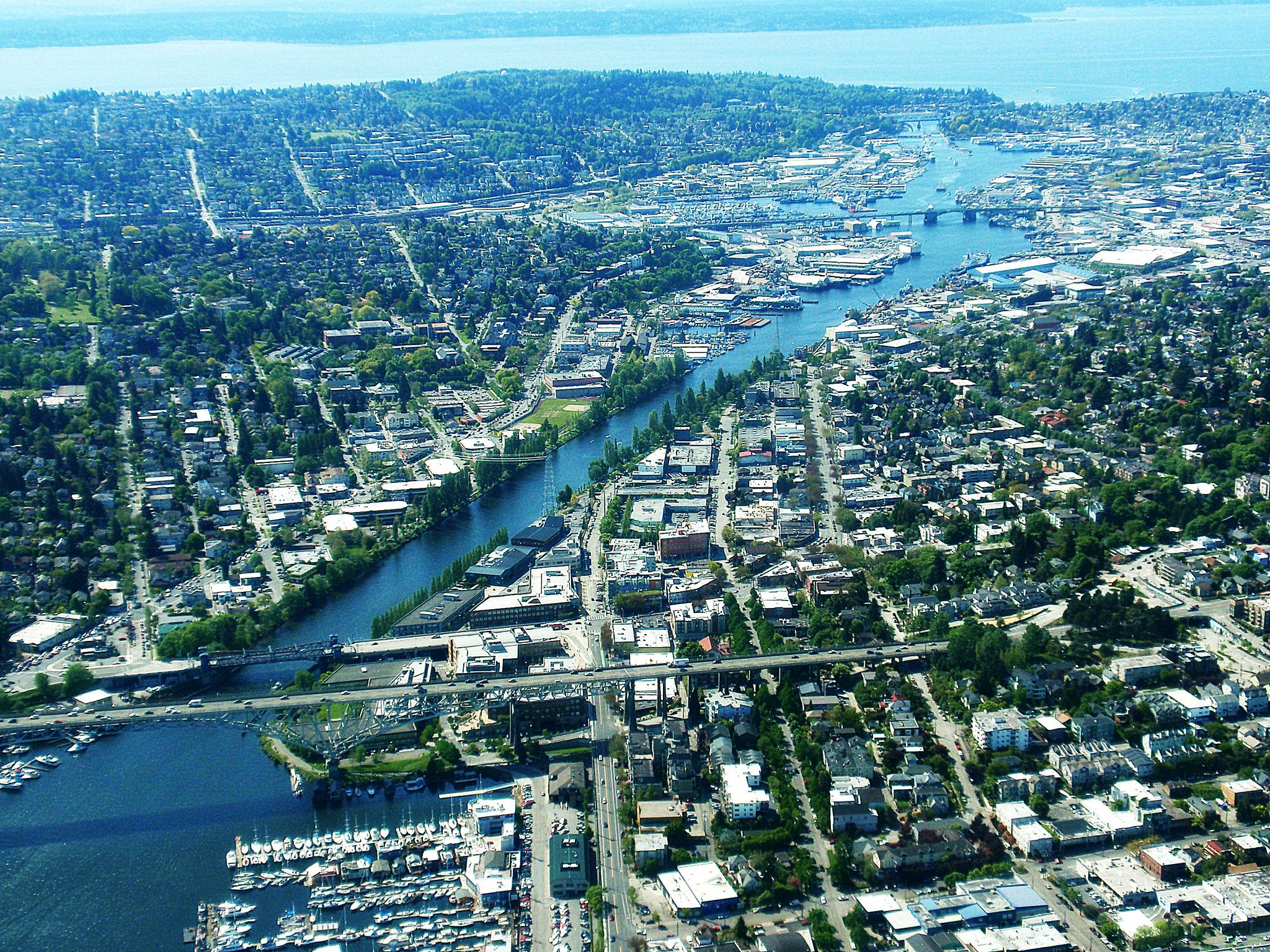 An aerial view of the ship canal with the Ballard Bridge in the distance surrounded by Seattle neighborhoods.