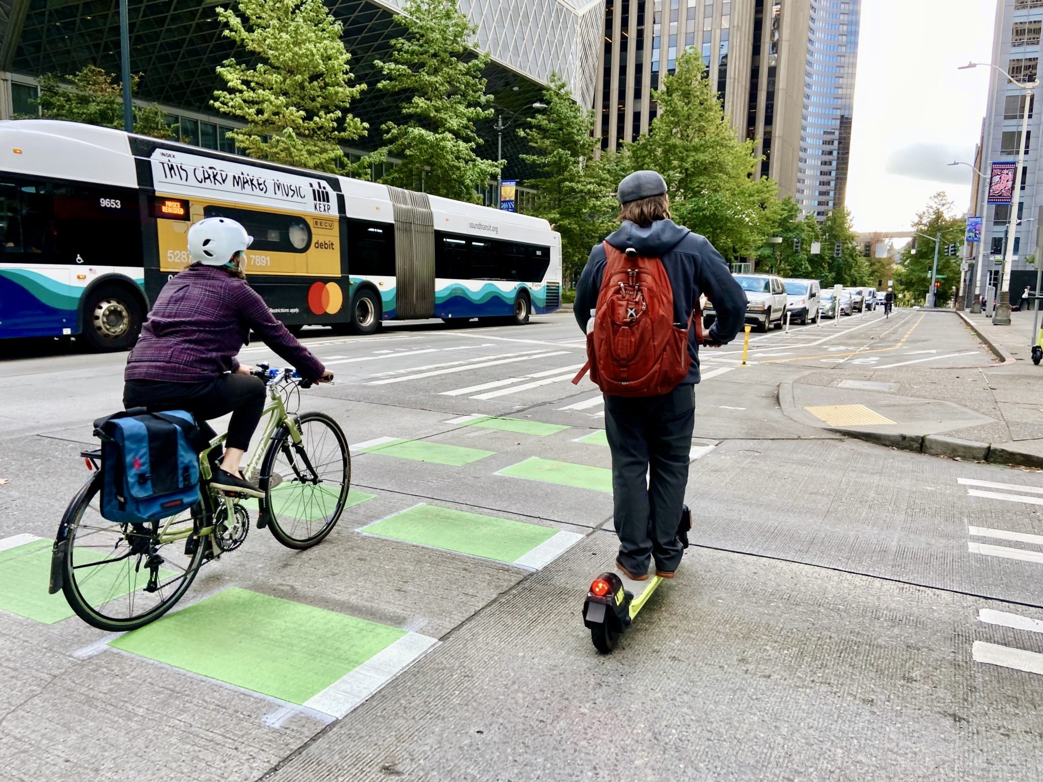 One person bikes and one person rides a scooter in a protected bike lane along 4th Ave in downtown Seattle.