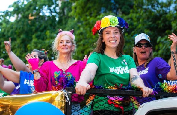 Several event-goers of a past Seattle Pride Parade smile at the event, wearing bright, colorful clothing.