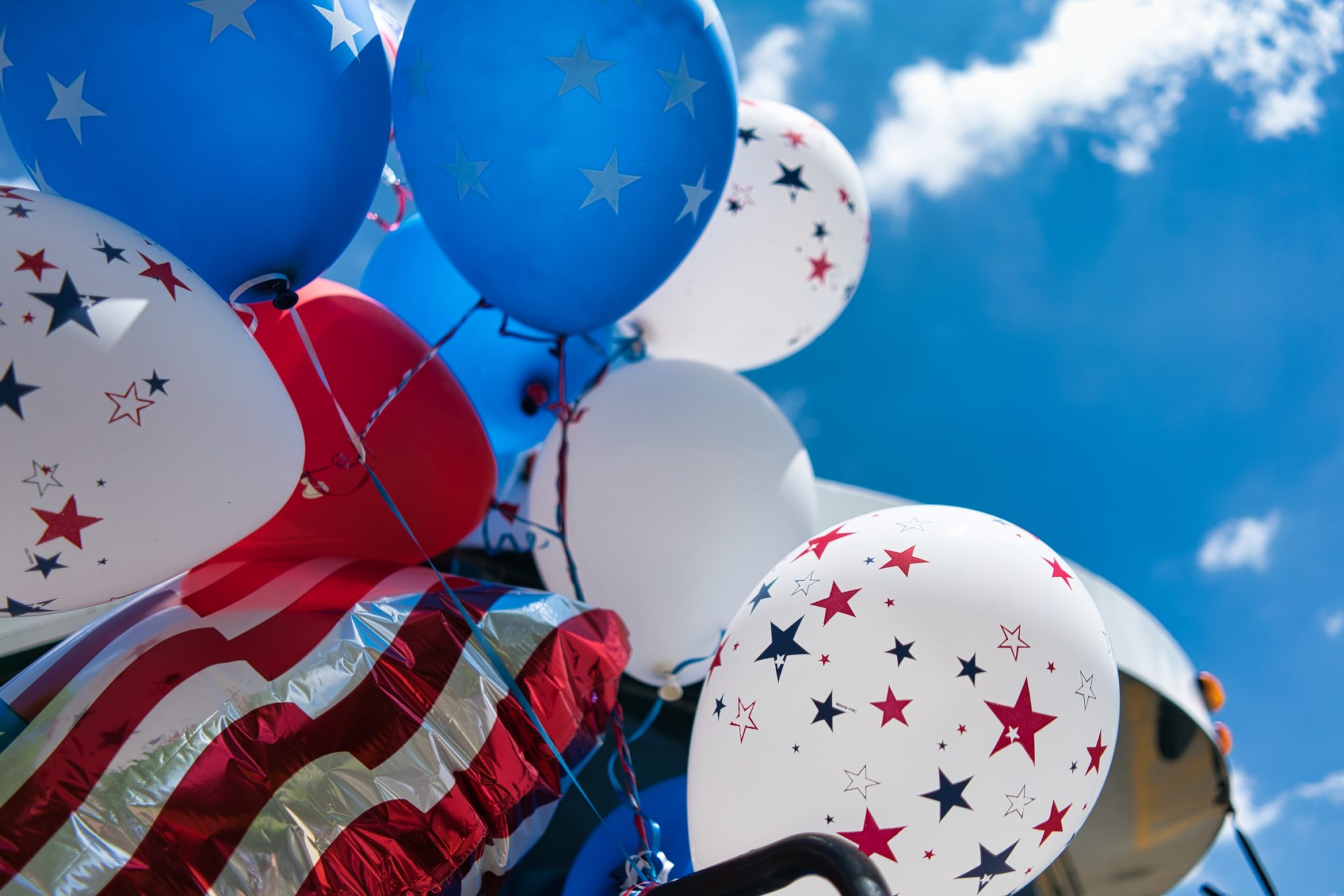 A photo of red, white, and blue balloons, looking upward toward a blue sky with white clouds.