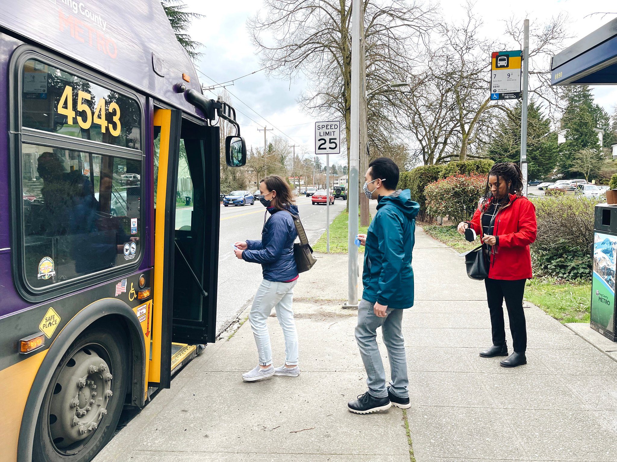 Three people get ready to board a King County Metro bus in southeast Seattle. The bus is on the left side of the photo with its doors open, and the people in the middle and right side of the photo, preparing to board.