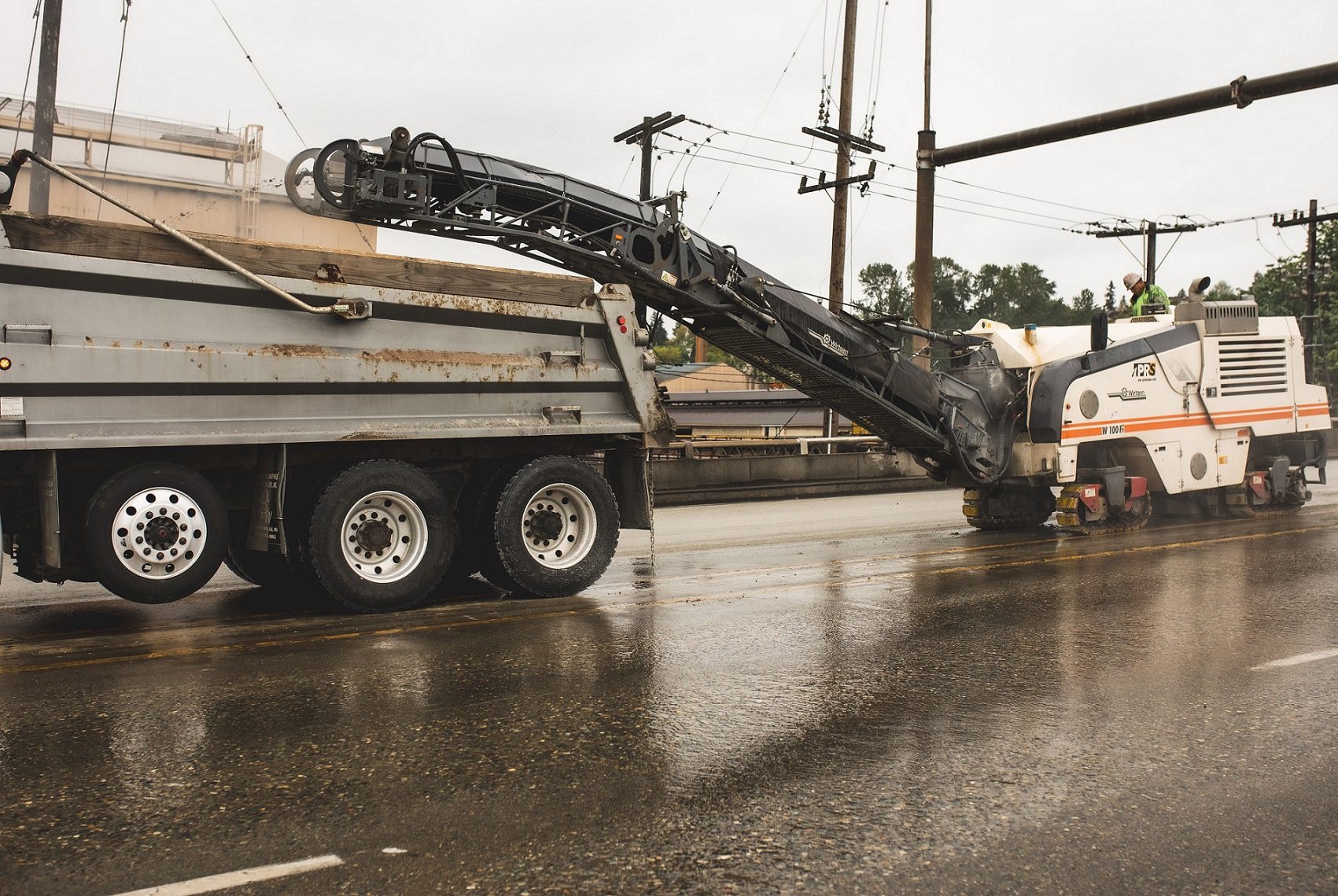 Crews conduct resurfacing along the Fauntleroy Expressway. Heavy equipment is pictured, including a large truck, on a wet and cloudy day.