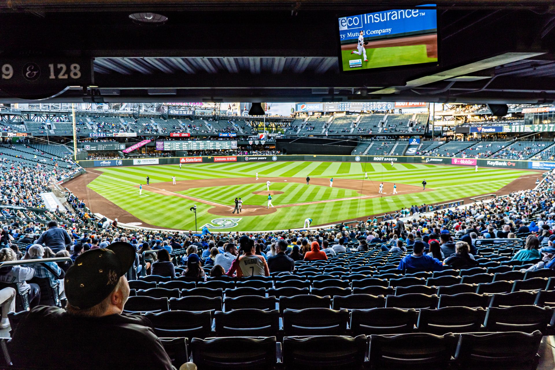T-Mobile Park during a Mariners home game. Fans watch the game taking place sitting in the lower seating area, on a sunny day.