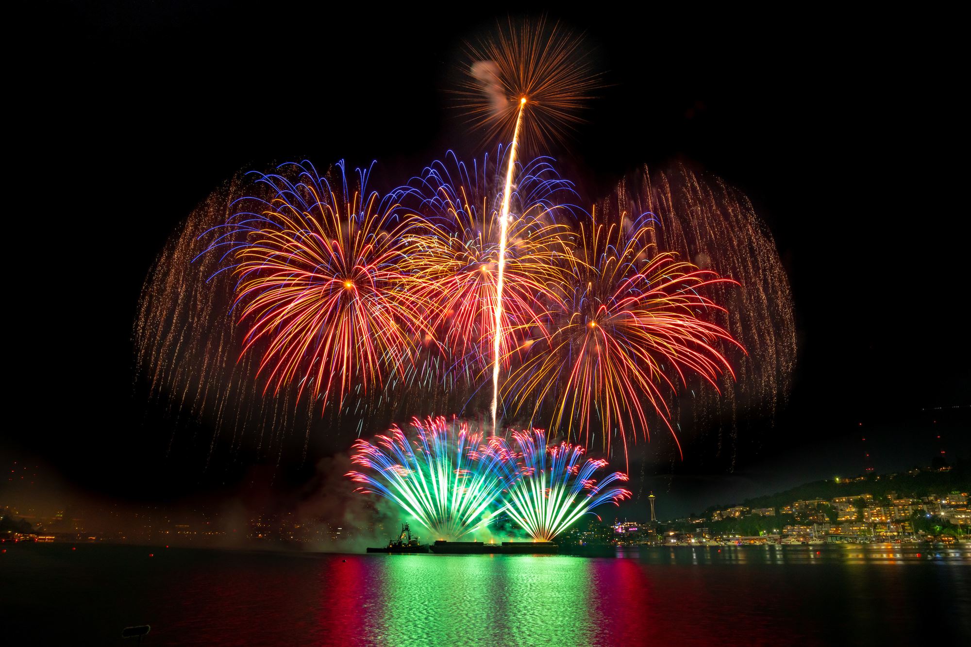 The fireworks show illuminates South Lake Union in Seattle. Colorful fireworks explode above the lake at night.
