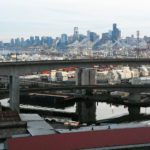 The West Seattle Bridge, with the city of Seattle visible in the background. The Duwamish Waterway and Port of Seattle equipment are also in the photo.