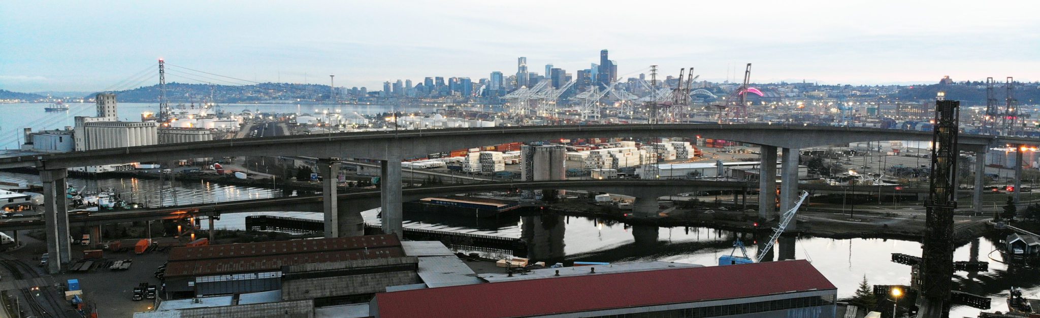 The West Seattle Bridge, with the city of Seattle visible in the background. The Duwamish Waterway and Port of Seattle equipment are also in the photo.