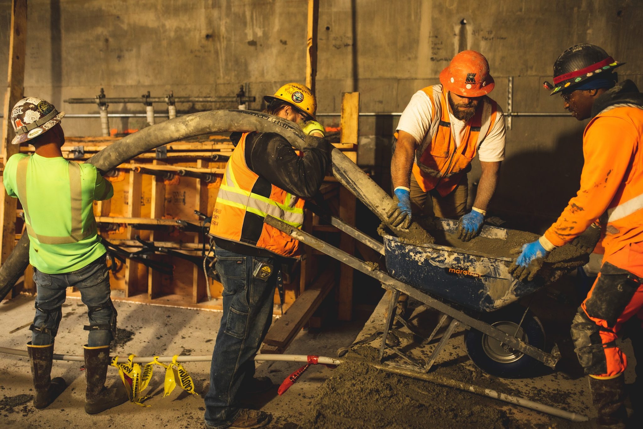 Construction workers pour concrete inside the West Seattle Bridge as part of the bridge repairs in May 2022. Four people in construction vests and hardhats work around a wheel barrow inside the bridge.