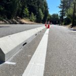 Photo of newly installed concrete along the protected bike lane at NE 40th St. White painted striping and orange cones are in the middle of the photo, with trees in the background.
