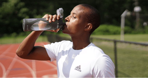 photo of person in a white shirt drinking water from a gray water bottle on a track.  