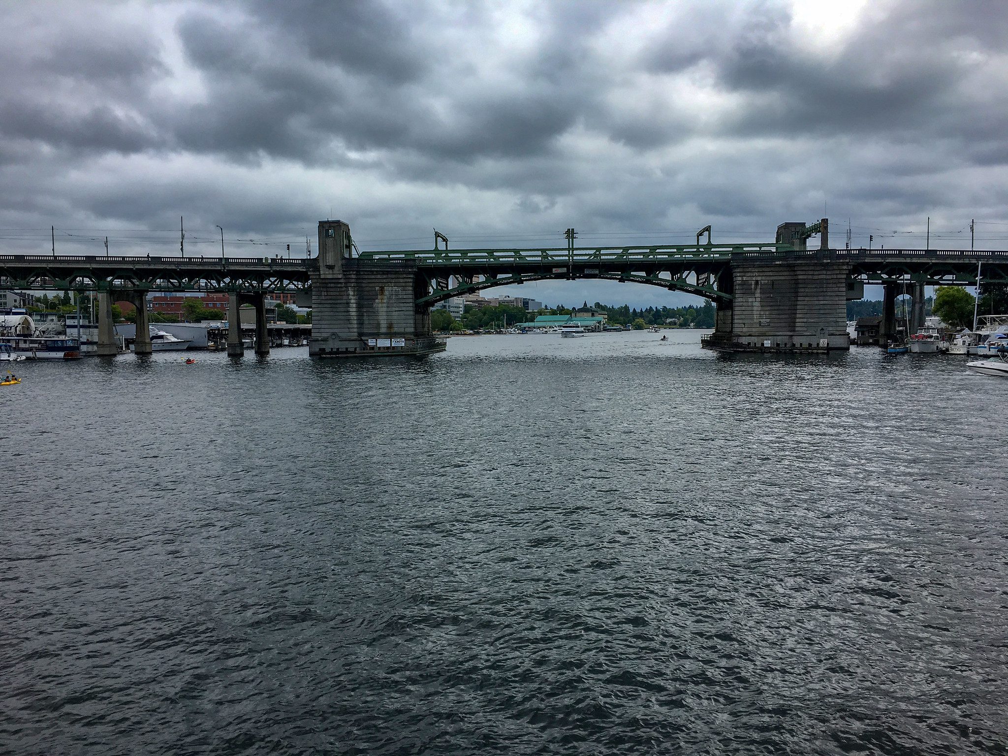 Photo of the University bridge taken from a boat on Lake Union, large body of water in front of the university bridge viewed from the side on a cloudy day.  