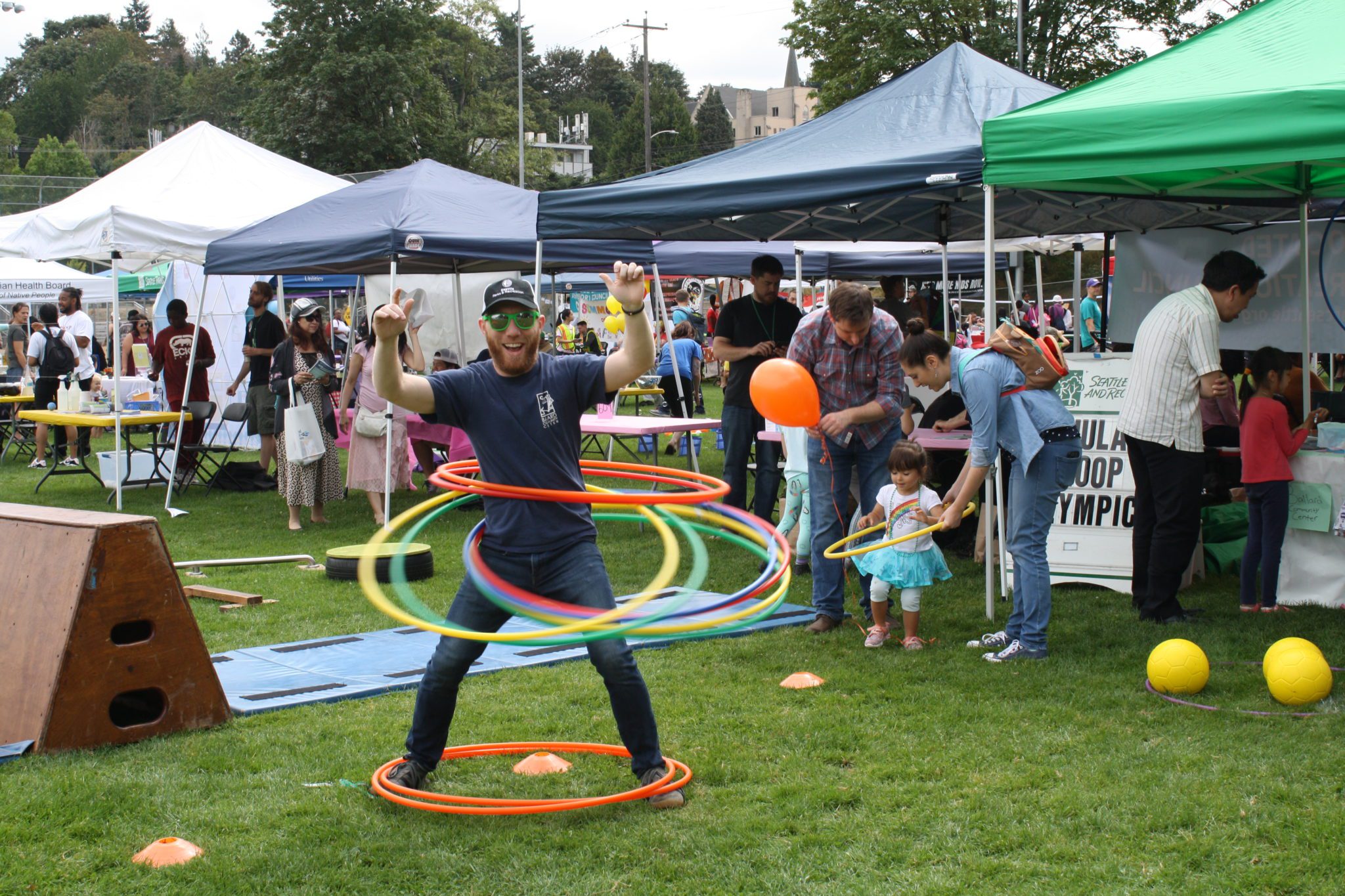A person hula-hoops near busy booths at a past Day of Play.