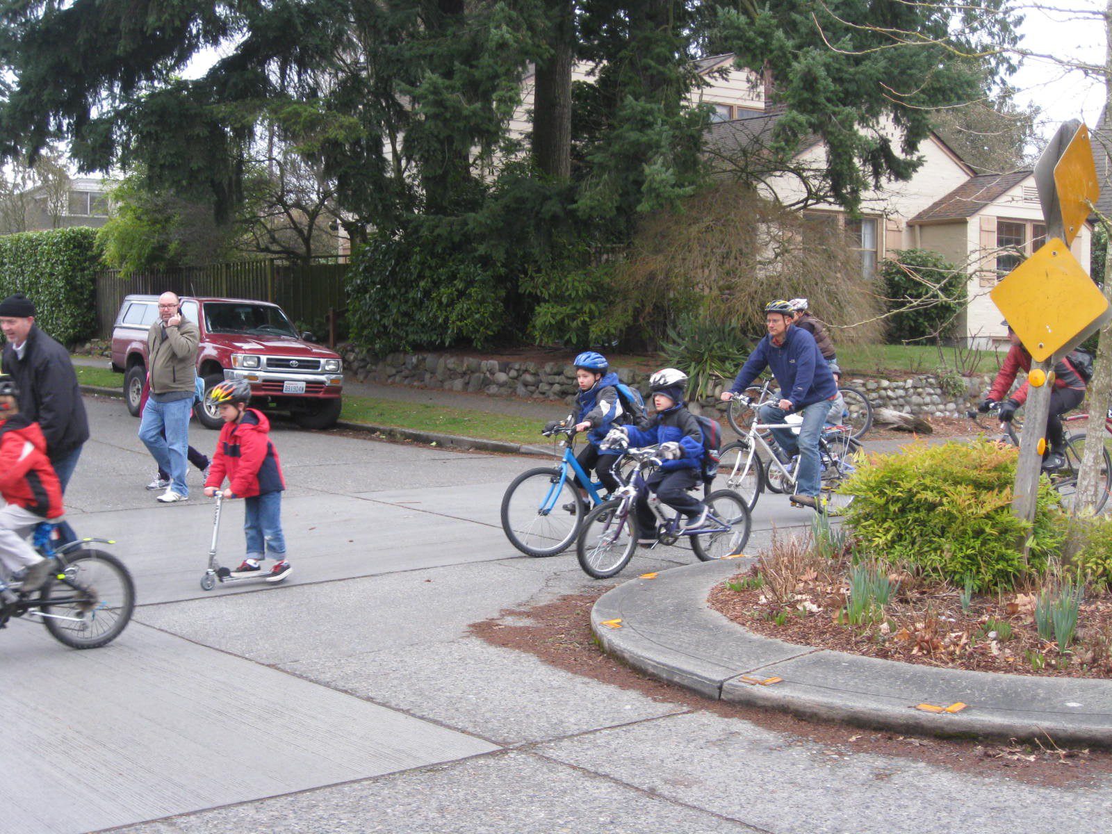 Students and parents riding their bikes to school around a traffic circle on a street.