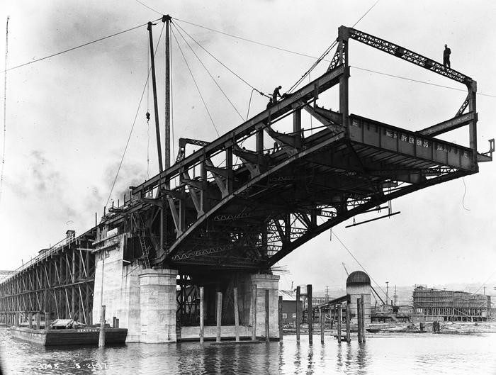 Black and white photo of the Ballard bridge during construction, half-way built with an open end shown at the front of the photo.  