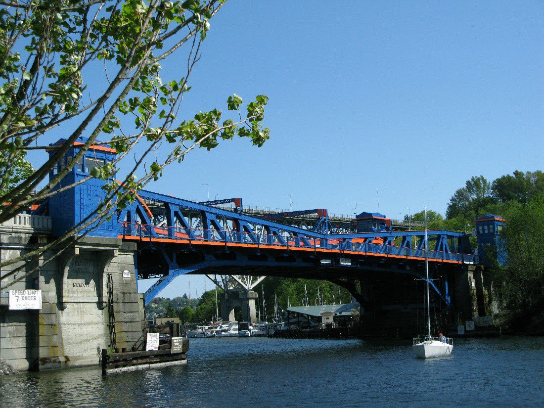Photo of the blue and orange Fremont bridge on clear day. A white boat is in the water under the bridge to the right corner.  