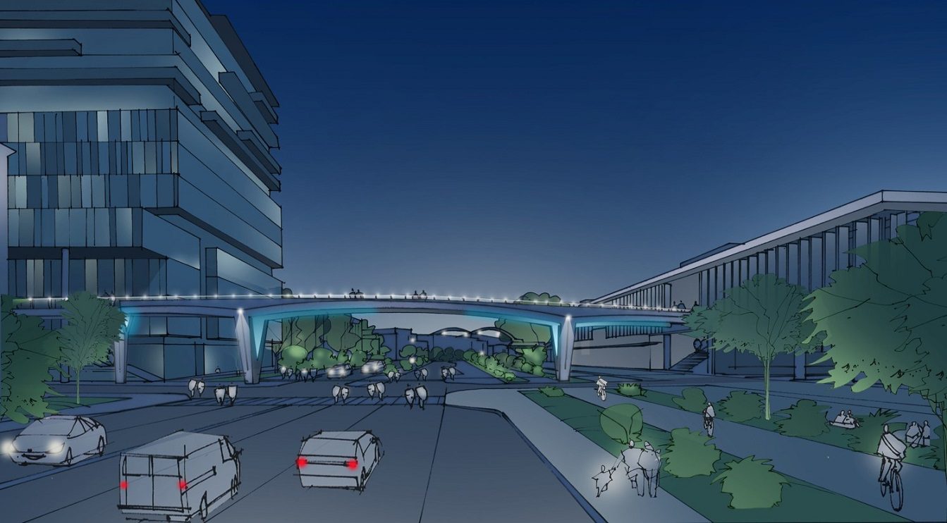 Artist’s rendering of new pedestrian bridge over Alaskan Way, upon completion, connecting pedestrians to the second level of the Colman Dock Entry Building. The rendering is shown in the late evening, with people walking and biking, vehicles, and large buildings, as well as trees and landscaping in green.
