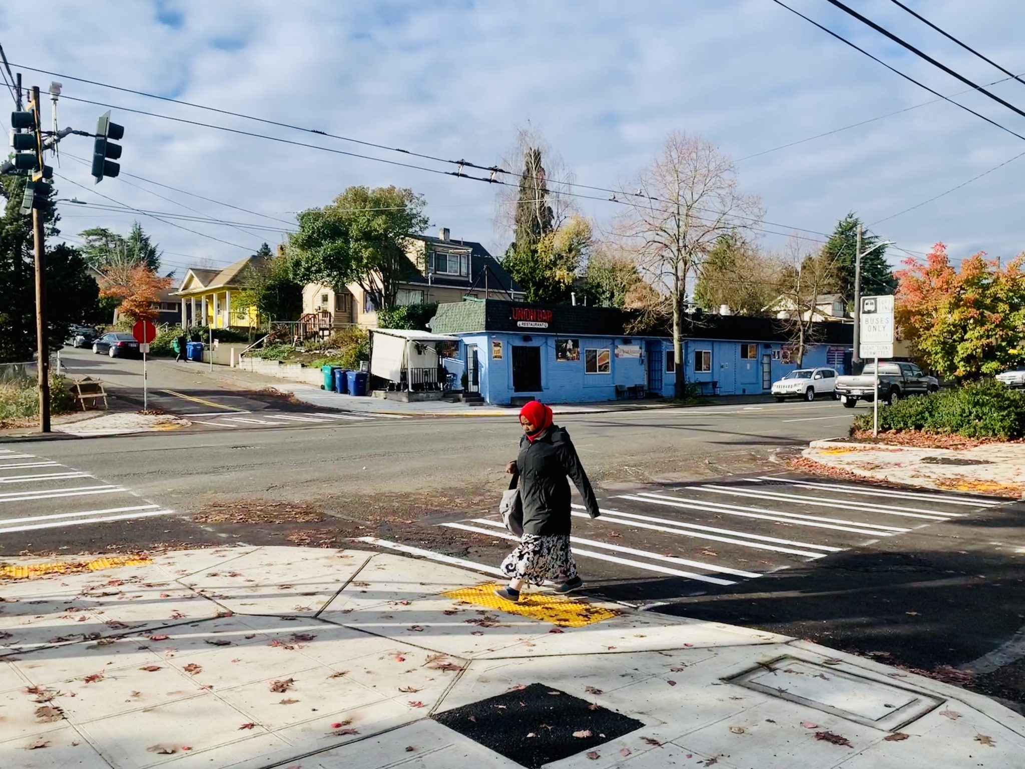 A person walks across the street, passing over a newly painted crosswalk and newly installed ADA curb ramps.  
