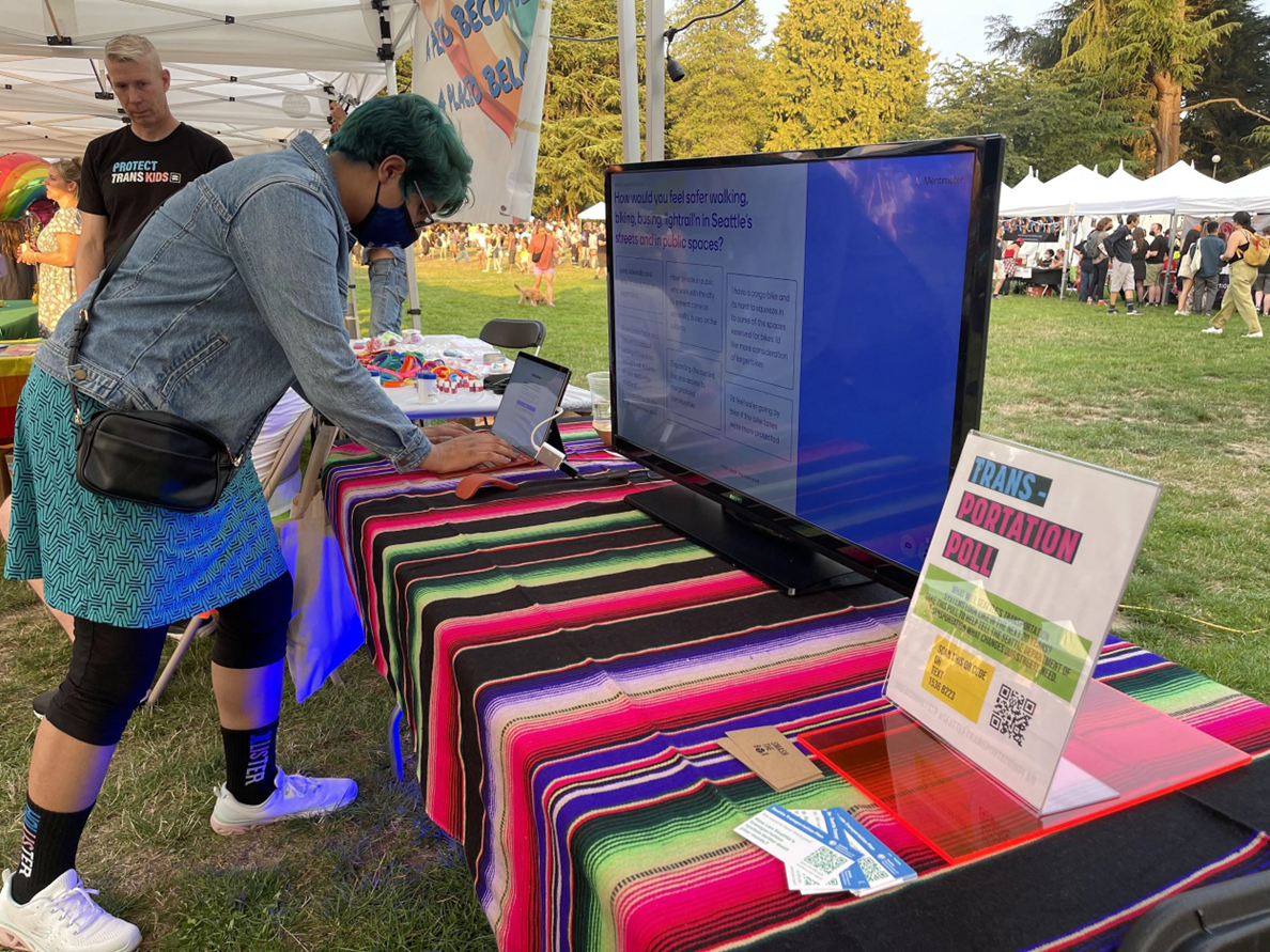 Table at Seattle Trans Pride 2022. Person is filling our a survey online at the table. Photo Credit: Yes Segura.