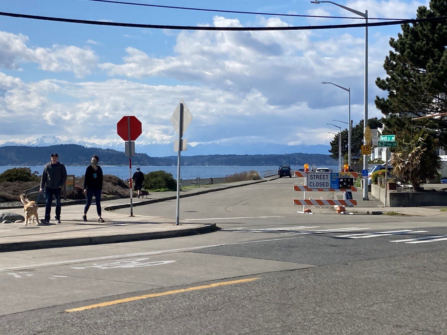 People walk along the entrance to the Alki Point Healthy Street on a sunny and cloudy day.