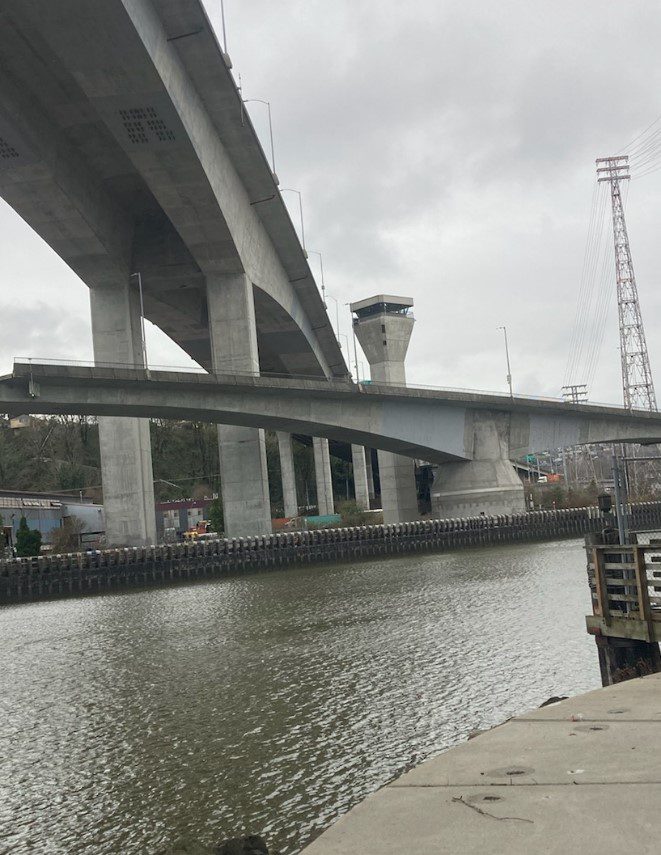 Photo of the Spokane St Swing Bridge open to marine traffic and closed to vehicle, bicycle, and pedestrian travelers. The Low Bridge and West Seattle High-Rise Bridge are in the upper part of the photo, with the Duwamish Waterway in the bottom part of the photo.