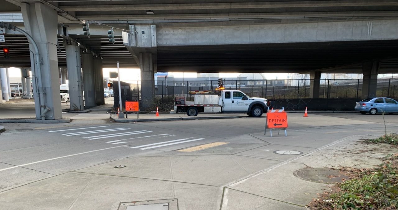 The S Spokane St Viaduct, with detour signs placed for people biking. A work truck is in the background, with streets and sidewalk in the foreground.