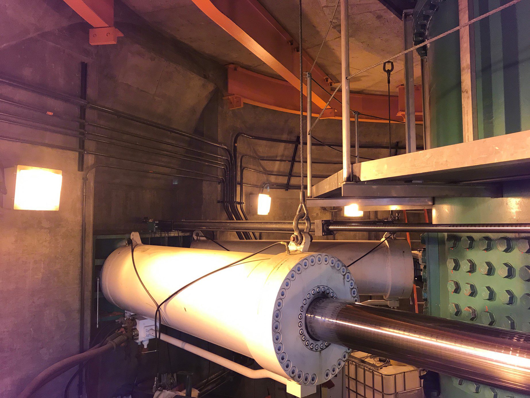 This 15,000-pound hydraulic cylinder is one of the largest parts of the complex system used to lift and turn the bridge so it can be opened for passing ships. The hydraulic cylinder is shown inside the bridge, with lights and other bridge equipment in the background.