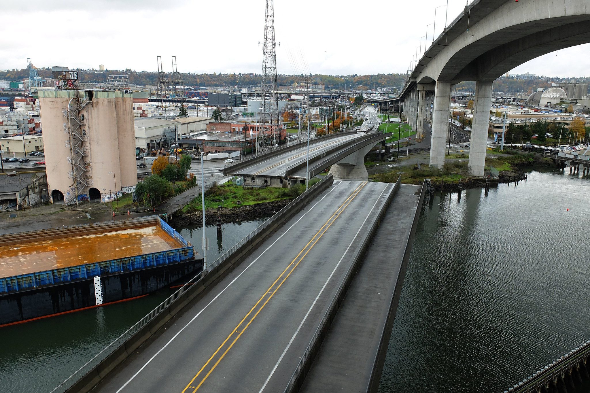 Previous photo of the Spokane St Swing Bridge across the Duwamish Waterway. The West Seattle High-Rise Bridge is in the upper-right corner, with various buildings in the upper left corner. A barge is in the lower left corner.