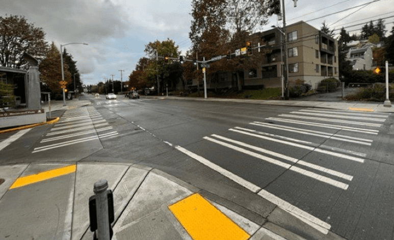 New intersection configuration at NE 74th St and Sand Point Way NE, near the entrance to Magnuson Park. The painted crosswalks extend from the sidewalk, with a traffic signal at the intersection.
