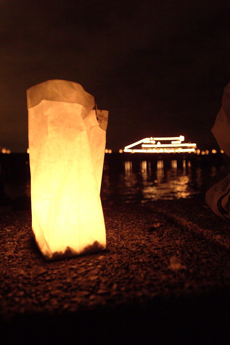 A bag with a candle in it illuminates the photo, with a large boat in the background.