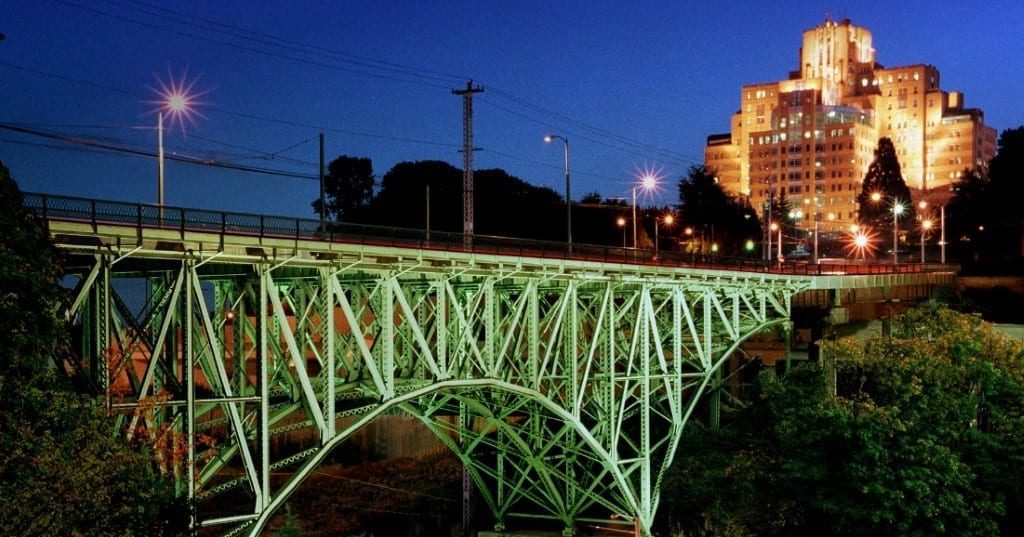 Photo of the Dr. Jose Rizal Bridge at night. The green bridge is illuminated, and a large building is in the upper right corner, also illuminated.