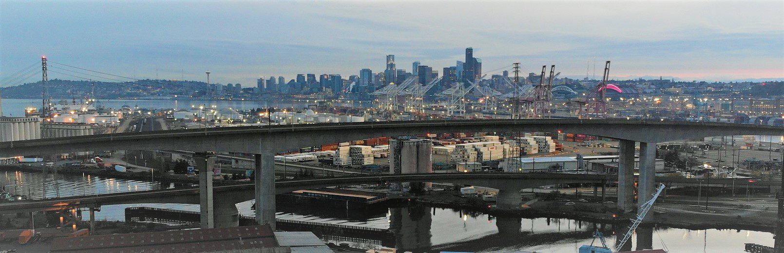 A north-facing photo with the West Seattle bridge in the foreground over water with the stadiums and the downtown Seattle skyline in the background.