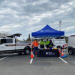 4 SDOT staff members stand under an SDOT-branded canopy in the event area, with two SDOT vehicles on either side of them.