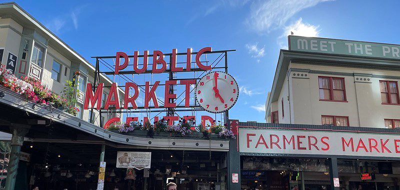 A photo of the Pike Place Public Market neon sign, angled upward toward a clear blue sky.