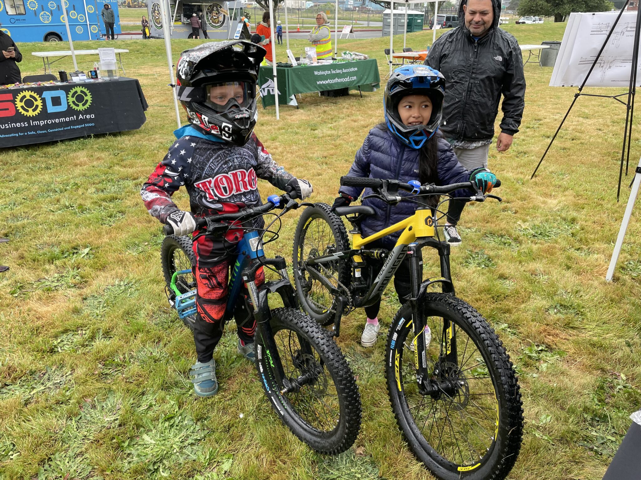 Two children wearing bike helmets stand with their mountain bikes at the SDOT booth, where they received free bike safety lights that attach to their handlebars.