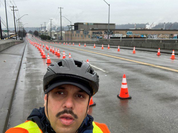Chief Transportation Officer, Venu Nemani, poses in front of cones that were delineating a temporary protected bicycle lane on a bridge