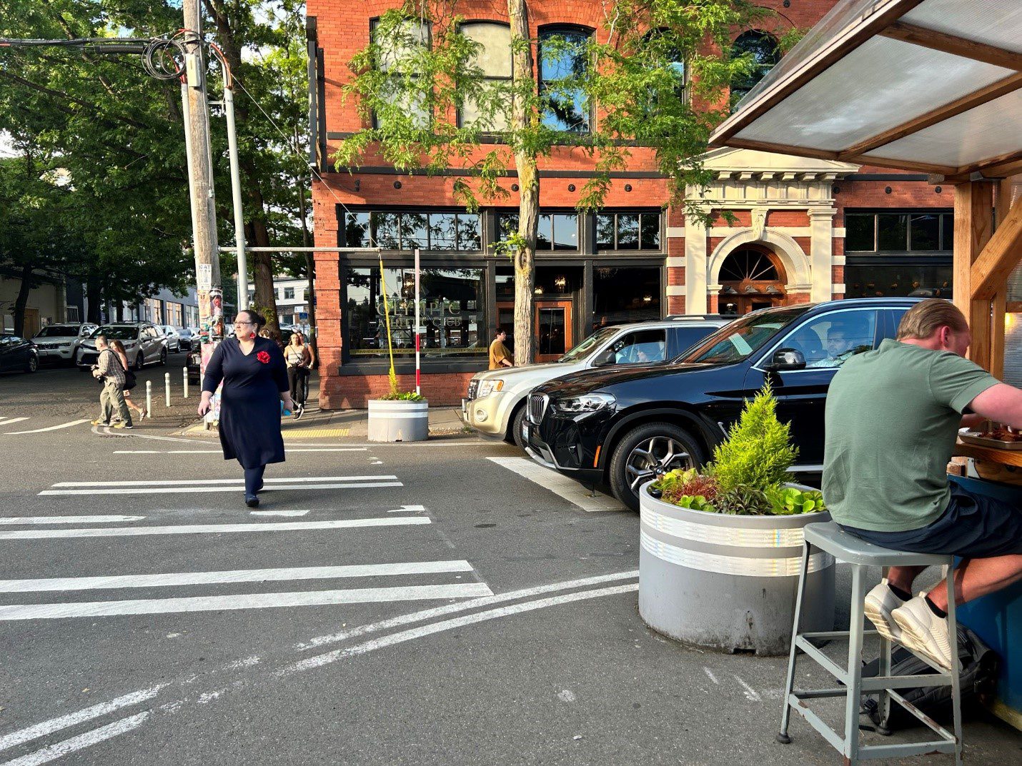 A person in a black dress uses a painted crosswalk to cross NW Vernon Place on Ballard Ave outside Olympic Athletic Club. 