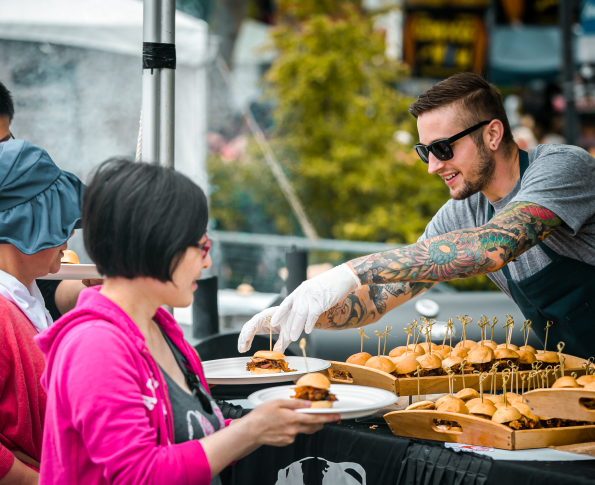 A vendor at Bite of Seattle puts small slider sandwiches on the plates of attendees.