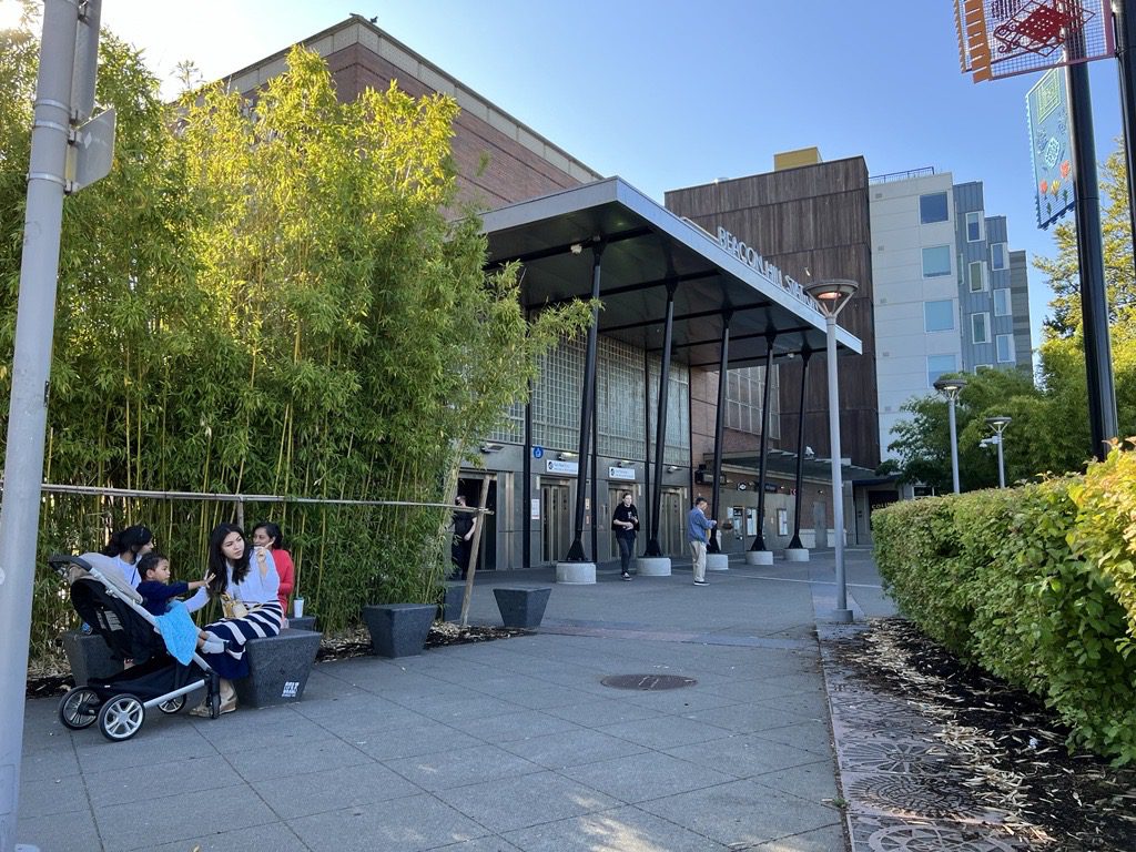 People sit on pedestrian seating outside the front entrance to the Beacon Hill light rail station.