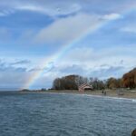 A photo of a rainbow arching over the beach and bathhouse at Golden Gardens Park.