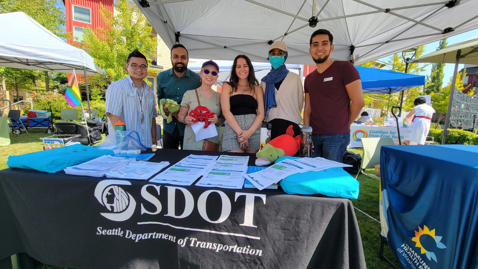 A group of 6 SDOT staff smile while standing behind an SDOT table at a community event.  