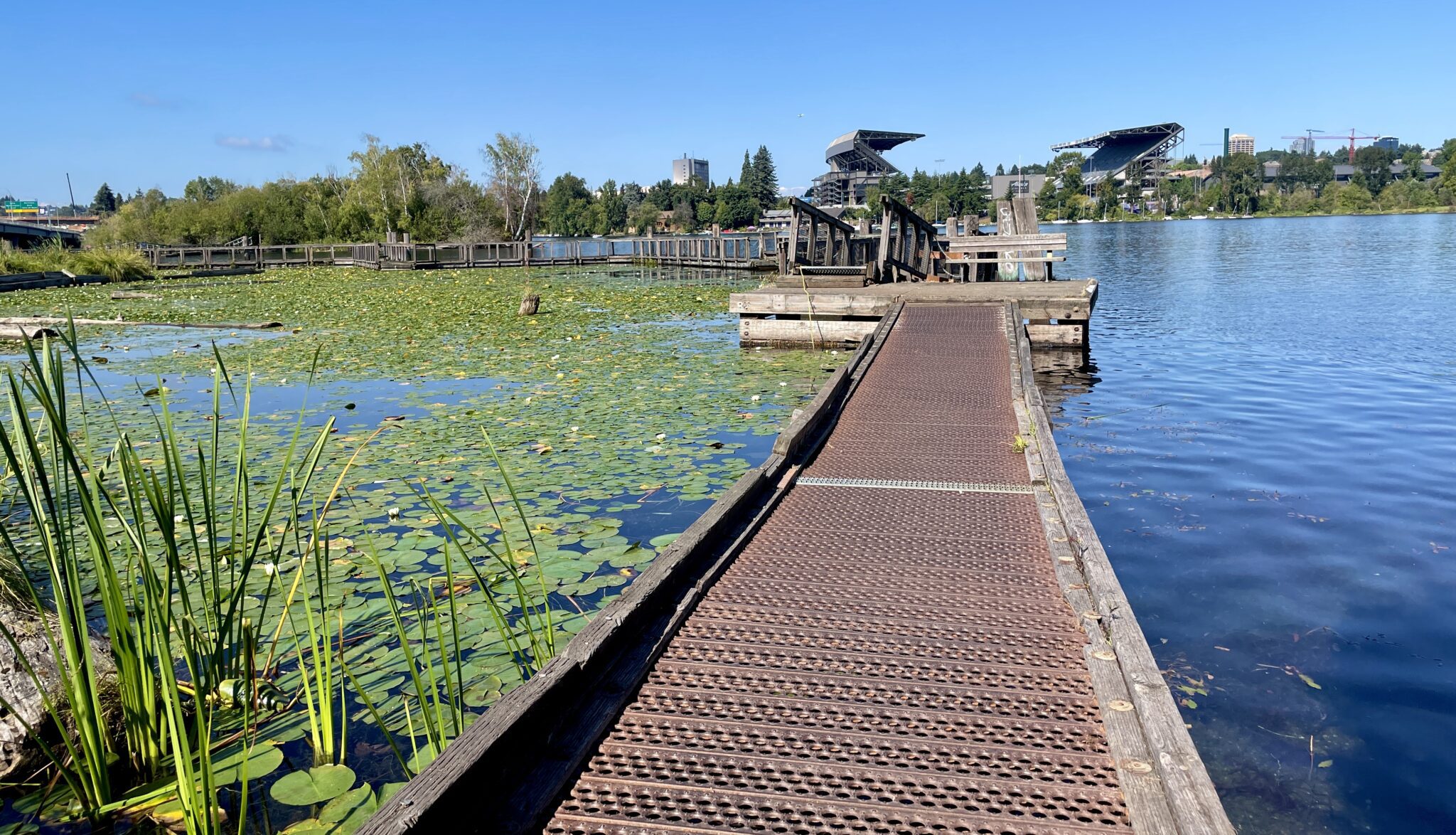 A wooden trail going over some water with a view of Husky Stadium in the background.