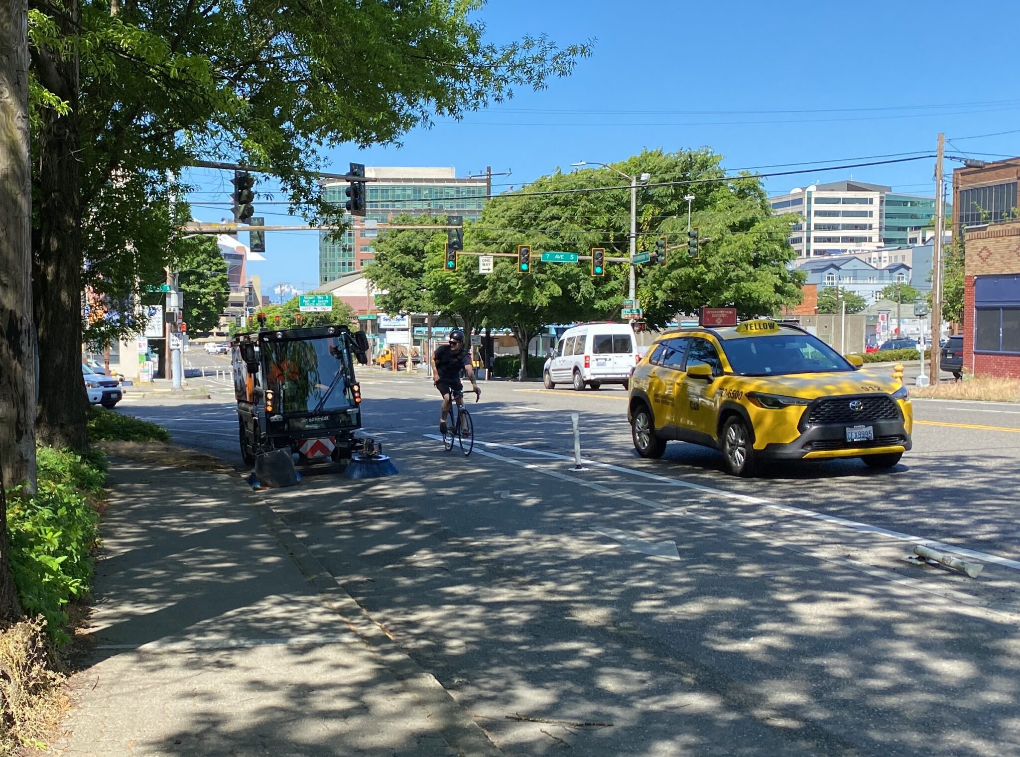 The electric sweeper in a bike lane clearing it of debris while a bicycle rider passes.