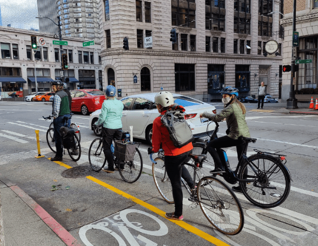 A group of four bicycle riders traveling down the 4th Ave protected bike lane.
