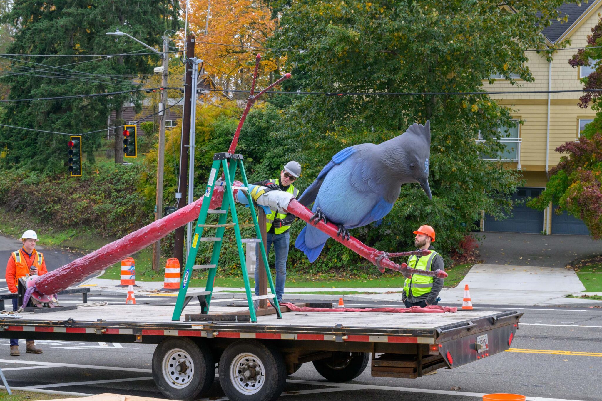 Three construction workers work to install the new piece of art, unloading it from a large flatbed truck.