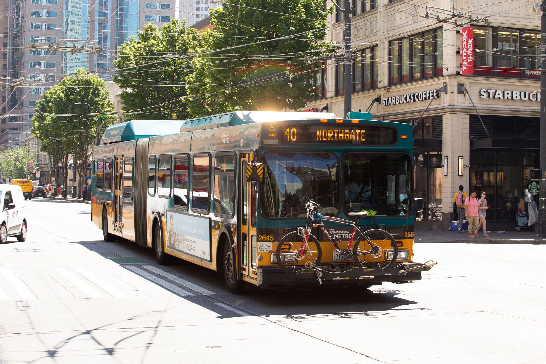 A bus travels down the street in front of large buildings on a sunny day.