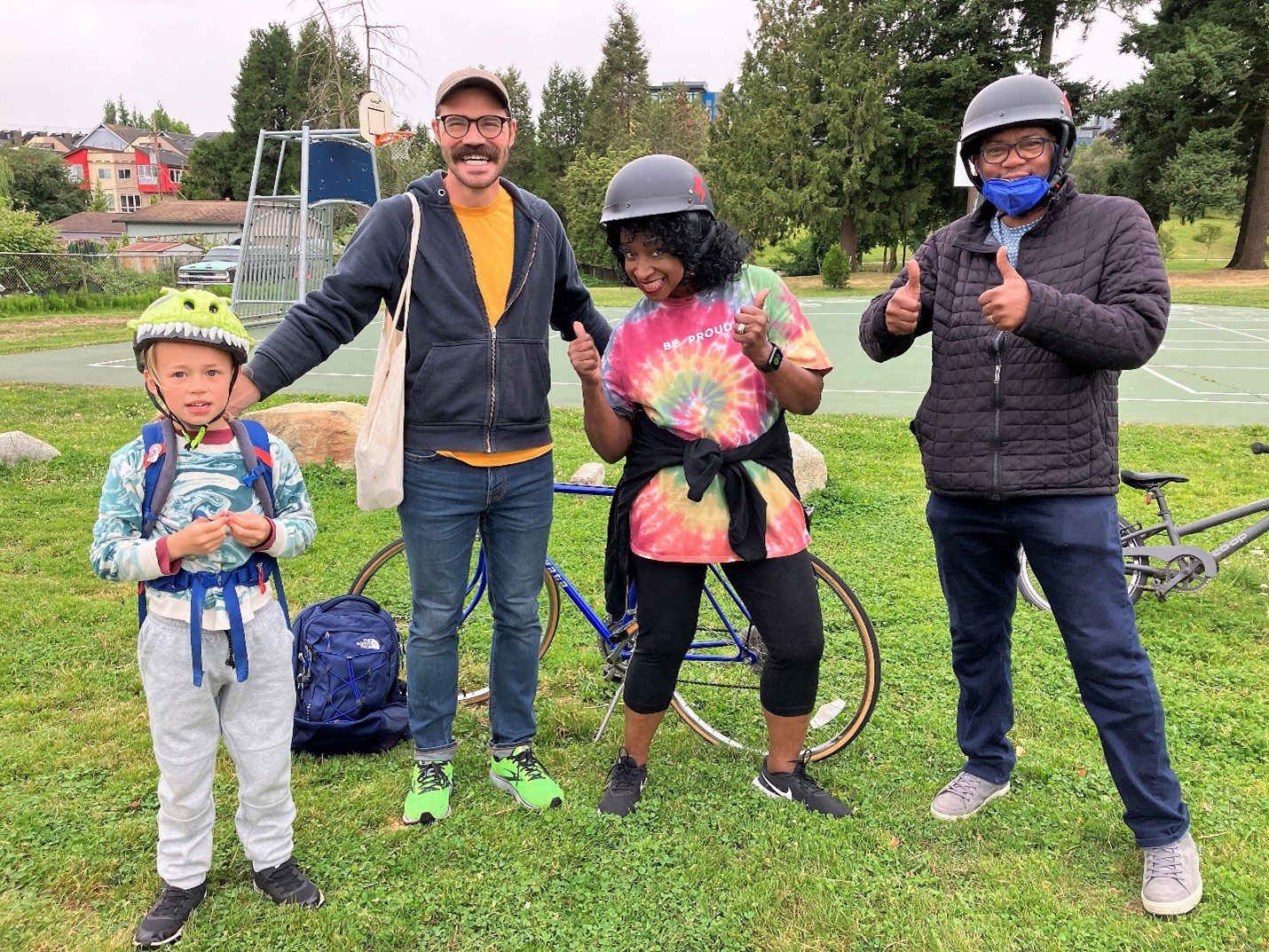 Four people post for a photo on a grassy field. A young person on the left wears a helmet, and the people are smiling.