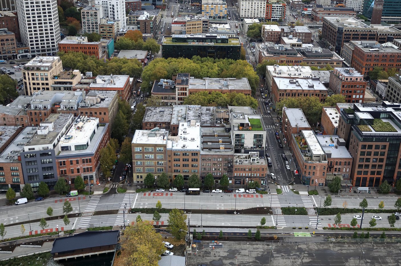 An aerial view of a cityscape with large buildings and street areas along with trees and vegetation.