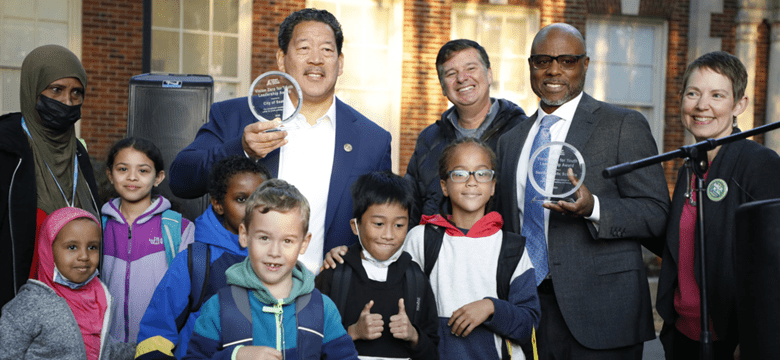 Photo of Mayor Bruce Harrell, SDOT Director Greg Spotts, and education leaders in Seattle and at the national level. Several kids smile at the camera on a sunny day.