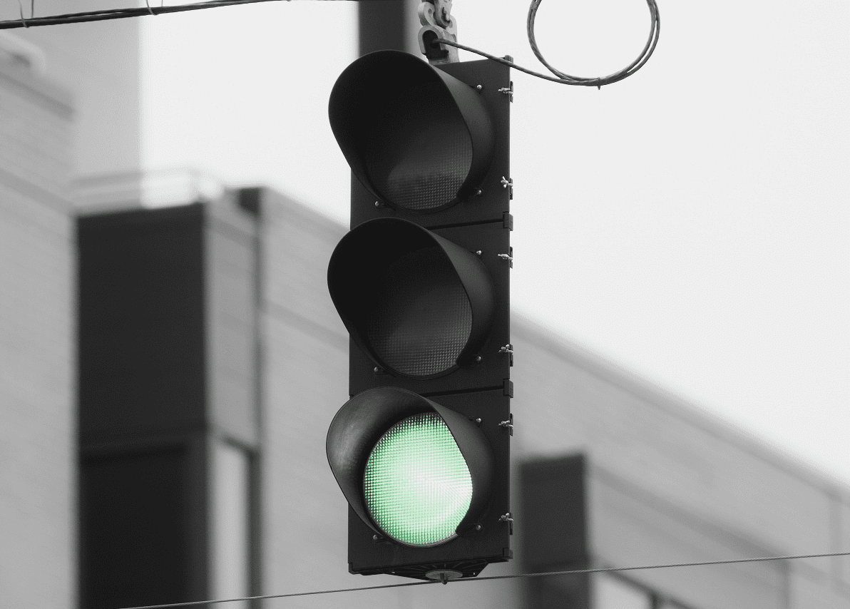 A green traffic light shines in a black-and-white photo. A large building is in the background.